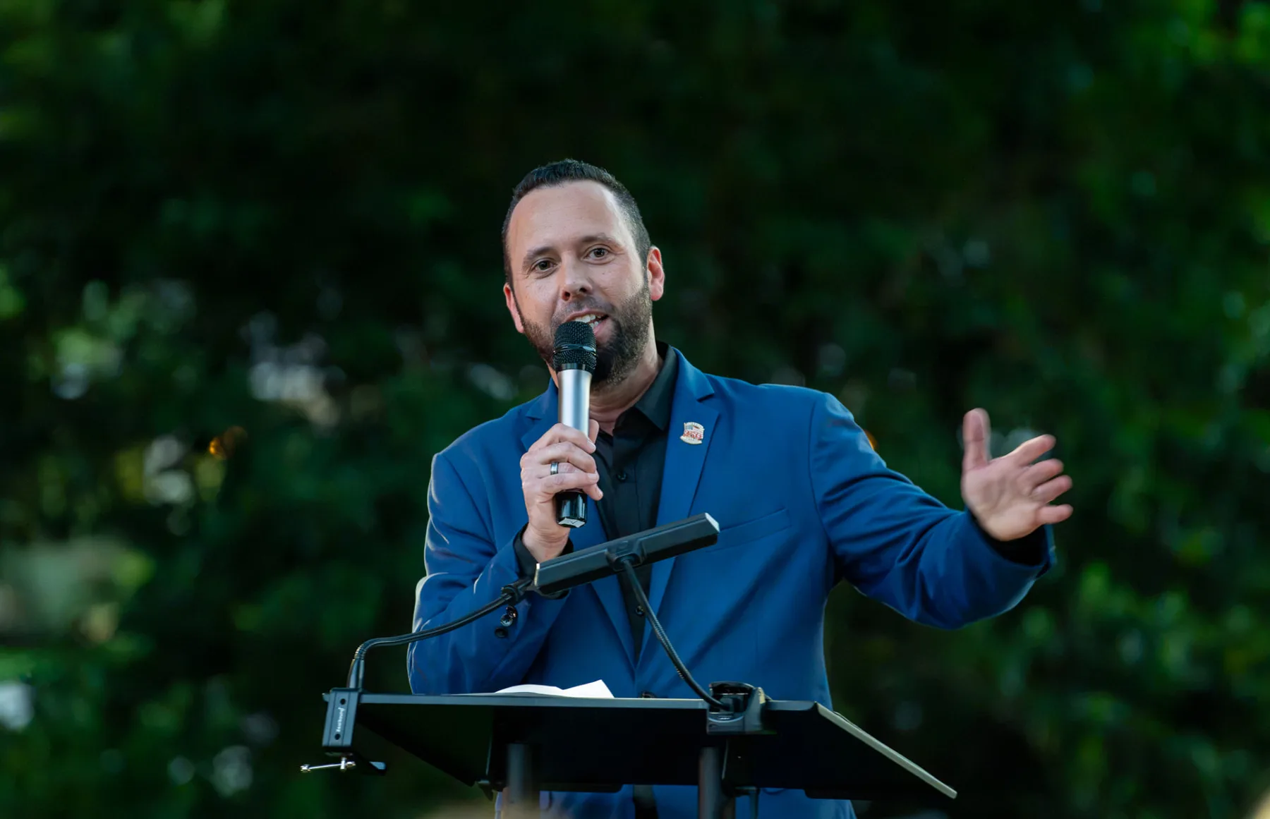 Austin Arthur, Event Chair, speaks into a microphone at the outdoor lectern.